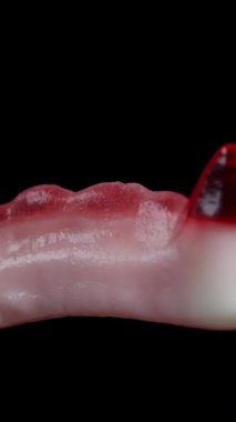 Dikey video. Kırmızı vampir dişleri şeklinde sakızlı şekerler, dönüşümlü. Siyah bir arkaplanda izole edilmiş.