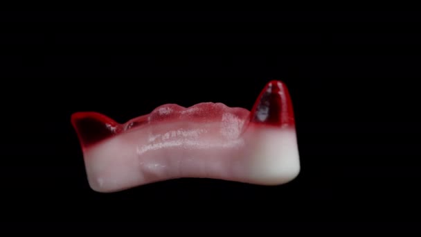 赤いヴァンパイアの牙の形をしたチューイ ガミーのキャンディ 黒い背景に孤立した — ストック動画
