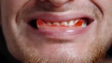 Genç sakallı bir adam ağzında kırmızı vampir dişleri şeklinde şeker tutuyor ve onları yiyor..