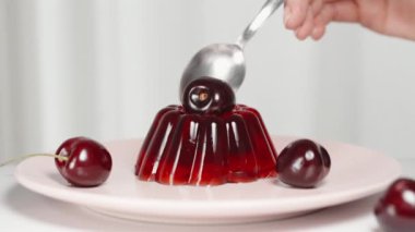Üstünde kiraz olan bir parça kırmızı jöleyi kaşıkla çıkarıyorum..