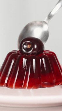 Dikey video. Üstünde kiraz olan bir parça kırmızı jöleyi kaşıkla çıkarıyorum..