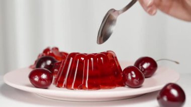 Bir parça kırmızı jöleyi kaşıkla kırdım, kirazlar tabağa saçılmıştı..