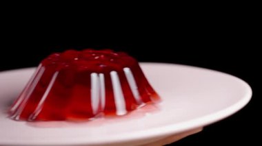 Elimde kırmızı ev yapımı jöle olan bir tabak getiriyorum ve üzerine bir kiraz koyuyorum, yavaş çekimde, yakın çekimde..