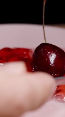 Dikey video. Kırmızı jöleyi kaşıkla, yavaş çekimde, yakın çekimde, kirazla topluyorum..
