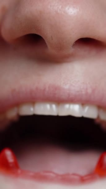 バーティカルビデオ 赤い吸血鬼の牙のような形をしたガミーキャンディーを食べる若い女性 クローズアップショット — ストック動画