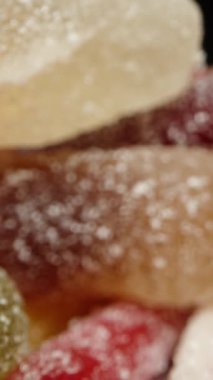 Çeşitli renkte, şekilli ve aromalı jelibonlar etrafa saçılmış ve kamera içeriden hareket ediyor. Dolly kaydırıcı aşırı yakın çekim.