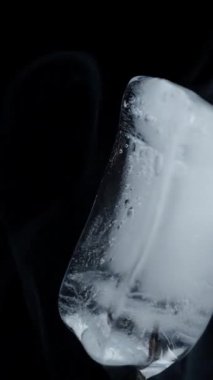 Bir buz küpü siyah bir zemin üzerinde döner, yakın plan çekimde duman yayar. İzole et