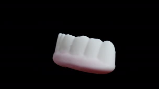 一种有粉红牙龈的白色牙齿形状的软糖 它在一个黑色的背景上旋转 孤立地 在一个特写镜头中 — 图库视频影像