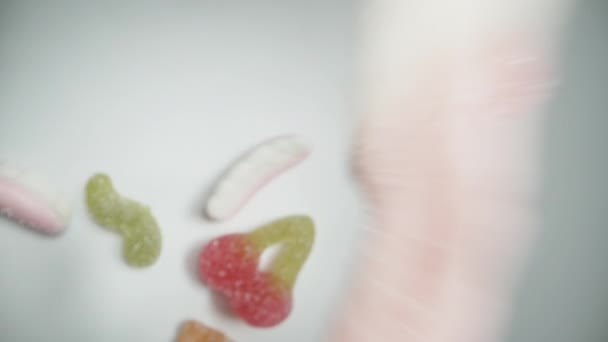 カメラは 歪んだガミーキャンディーの混合物が上から白いテーブルに落ちてゆっくりと降下します ドリー ショット — ストック動画