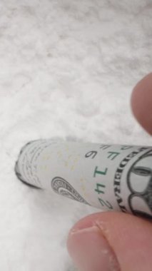 Dikey video. 100 dolarlık banknotu yuvarlayarak beyaz tozu içine sokuyorum. Uyuşturucu kullanımı ve kokain kavramı. Dolly kaydırıcı aşırı yakın çekim.