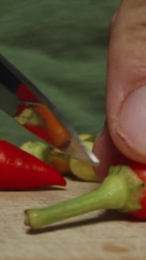 Dikey video. Kamera ahşap tahta boyunca geriye doğru süzülüyor, çok renkli kırmızı biberlerin filizlerini keserken yakından çekiyor..