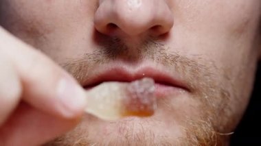 Sakallı bir adam, yakın planda, kola şişesi şeklinde marmelat şekeri yiyor..