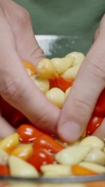 Dikey video. Çok renkli mini biberleri yavaş çekimde, bir kase suda yıkayan ellerin yakın çekimi..