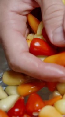 Dikey video. Erkek eller çok renkli mini biberleri suda yıkıyor, yavaş çekimde, su sıçratarak. Kapat.