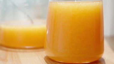 Bir bardak portakal suyu, arkaplanda güneş ve bir sürahi meyve suyu var..