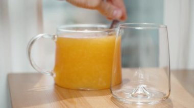 Arka planda boş bir bardak ve bir sürahi portakal suyu, karıştırmak ve dökmek için bir kaşık kullanıyorum, ağır çekimde..