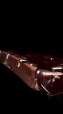 Dikey video. Siyah arka planda, erimiş çikolata damlacıkları damlayan siyah bir çikolata..