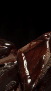 Dikey video. Siyah bir arka planda dönen çikolata kareleri ve fındıklar yığınına yakın çekim.