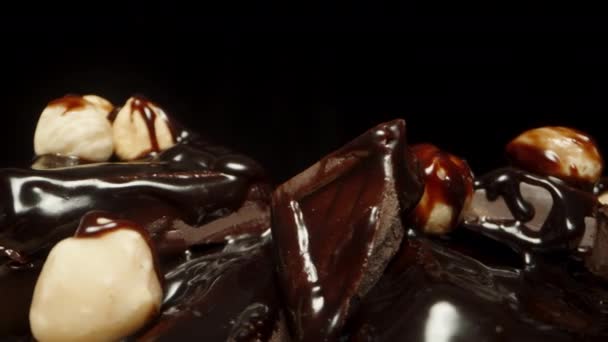 黒い背景に回転するチョコレート正方形とヘーゼルナッツのマウンドのクローズアップ — ストック動画
