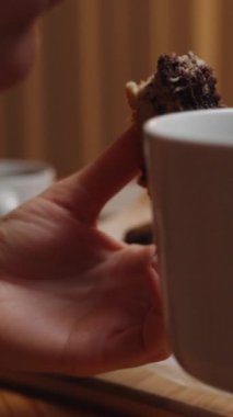 Dikey video. Genç bayan odanın sıcak ışığında bir bardak ev yapımı mermer pastayla çay içmeyi sever..