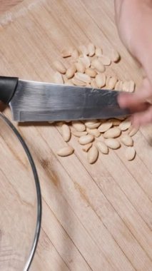 Dikey video. Üst Manzara: Bir kadın ev yapımı granola hazırlıyor, fıstık doğruyor.