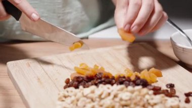 Bir kadın ev yapımı granola hazırlıyor, malzemeleri doğruyor ve kurutulmuş kayısıları kesiyor..