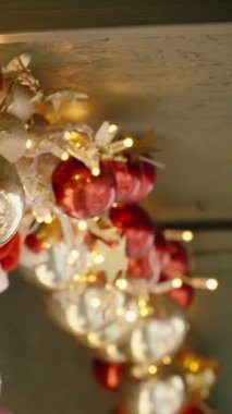 Dikey video. Altın ve kırmızı Noel ağacı süsleri ahşap evin saçaklarında asılı. Yakın çekim görünümü.