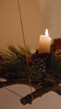 Dikey video. Bu Noel enstalini mumlar ve daldaki Noel süsleri ile kendimiz yaptık. Sıcak ve şenlikli bir ev atmosferi yaratır..