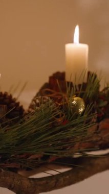 Dikey video. Duvarda, Noel süsleri ve mum tutacakları olan el yapımı bir kurulum var..