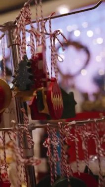 Dikey video. Geniş çeşitliliğe sahip bir mağazada el yapımı Noel süslemeleri yapan genç bir kadın, arka planda Bokeh 'in çelengi ile birlikte onları inceliyor..