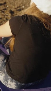 Dikey video. Şafakta sakin deniz, yeni yıl sabahı, Noel Baba şapkalı bir kadın suya taş atıyor..