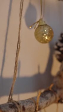 Dikey video. Bir kadın Noel için evini kozalak ve Noel süsleriyle süslenmiş ev yapımı dallarla süslüyor..