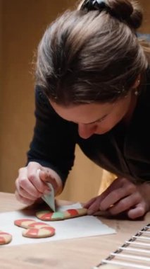 Dikey video. Sıcak bir Noel arifesinde, genç bir kadın şekerleme şeklinde zencefilli kurabiyeleri kremayla süslüyor..