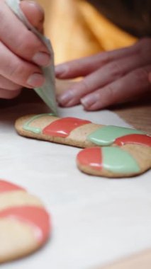 Dikey video. Bir kadın pasta torbasından zencefilli kurabiyeye renkli krema döküyor..