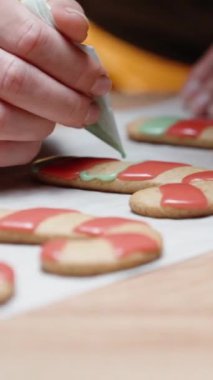 Dikey video. Hassas çizgiler kullanarak, kadın zencefilli kurabiyenin üzerine yeşil krema döküp yakın çekim görüntüsüyle dolduruyor..