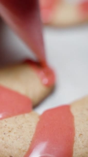 バーティカルビデオ 小さなペストリーバッグを使用して 女性はキャンディーケーンの形をしたジンジャーブレッドクッキーに赤いアイシングを適用します クローズアップショット — ストック動画