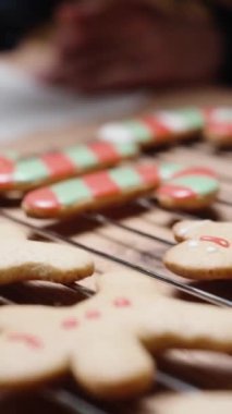 Dikey video. Ev yapımı zencefilli kurabiyeleri şeker kamışları ve küçük insanlar şeklinde hazırlayan kadın, onları kremayla süslüyor..