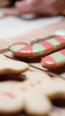 Dikey video. Küçük bir torbadan beyaz krema kullanan kadın, zencefilli kurabiyeyi baston şekeri şeklinde kaplıyor..