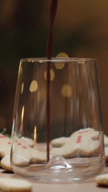 Dikey video. Noel arifesi, bir çelengin arka planında sıcak kakao bardağa dökülüyor. Yavaş çekimde yakın çekim. Mumlar ve şekerler masaya saçıldı..