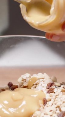 Dikey video. Bir kadın ev yapımı granola yapıyor. Tahıl ve fındıklara elma püresi ekliyor..