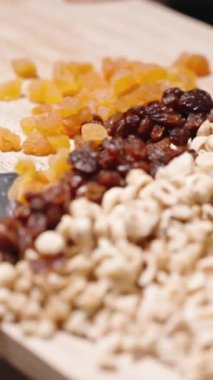 Dikey video. Kadın ev yapımı granola malzemelerini kesmiş ve ağır çekimde bir kaseye koyuyor..