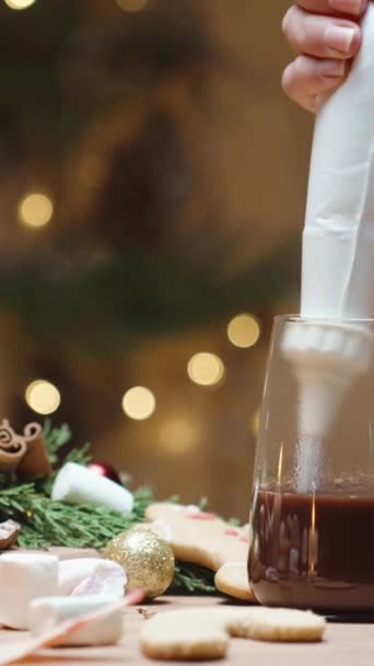 バーティカルビデオ ホーム クリスマスインテリア テーブルの上のお菓子 そして女性はカカオにペストリーバッグからホイップクリームを絞ります — ストック動画
