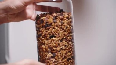 Kadın yeni yapılmış granola ile dolu cam bir kavanozu sallıyor. Yavaş çekim.