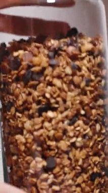 Dikey video. Kadın yeni yapılmış granola ile dolu cam bir kavanozu sallıyor. Yavaş çekim.