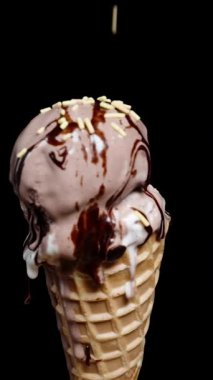 Dikey video. Dondurma kepçeli waffle külahı renkli şeker parçacıkları serpiştirilir, ağır çekimde döner..