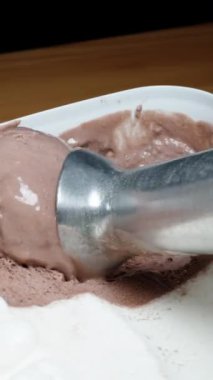 Dikey video. Farklı renkte ve aromalı dondurma kabında özel bir kaşık kullanarak bir top çikolata çıkarıyorum..