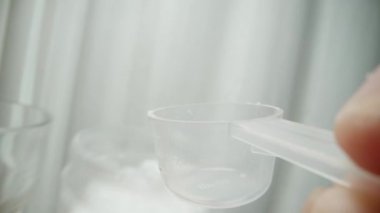 Birinci şahıs makro video: Bir ölçüm kaşığı tutarak, kavanozdan beyaz toz topluyorum ve bardağa döküyorum. Spor ek konsepti.