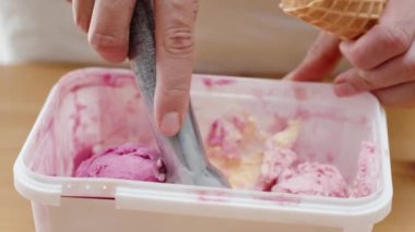 Kadın bir kepçe pembe dondurmayı özel bir kaşıkla yuvarlar ve waffle külahına koyar..