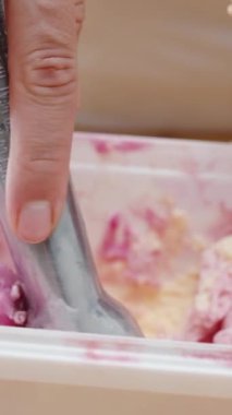 Dikey video. Kadın bir kepçe pembe dondurmayı özel bir kaşıkla yuvarlar ve waffle külahına koyar..