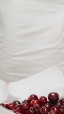 Kadın bir tabak kirazın üzerindeki çukurları temizlemeye çalışıyor. Dikey video.